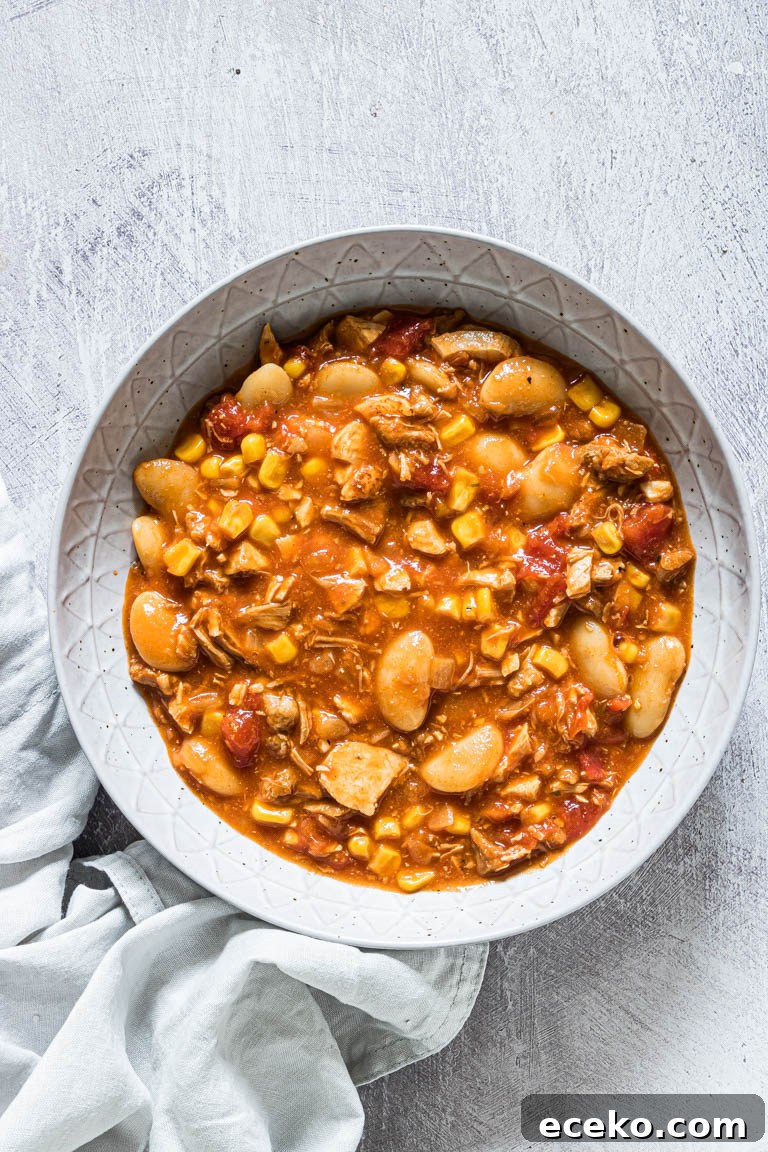 a serving of brunswick stew in a ceramic bowl set next to a cloth napkin