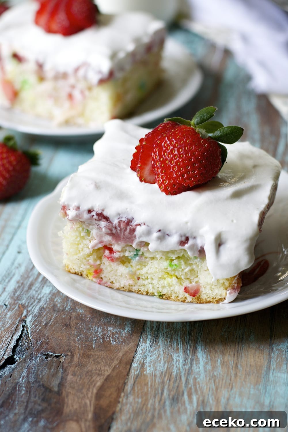close up of a slice of strawberry funfetti cake on a white plate. Another cake slice is in the background. 