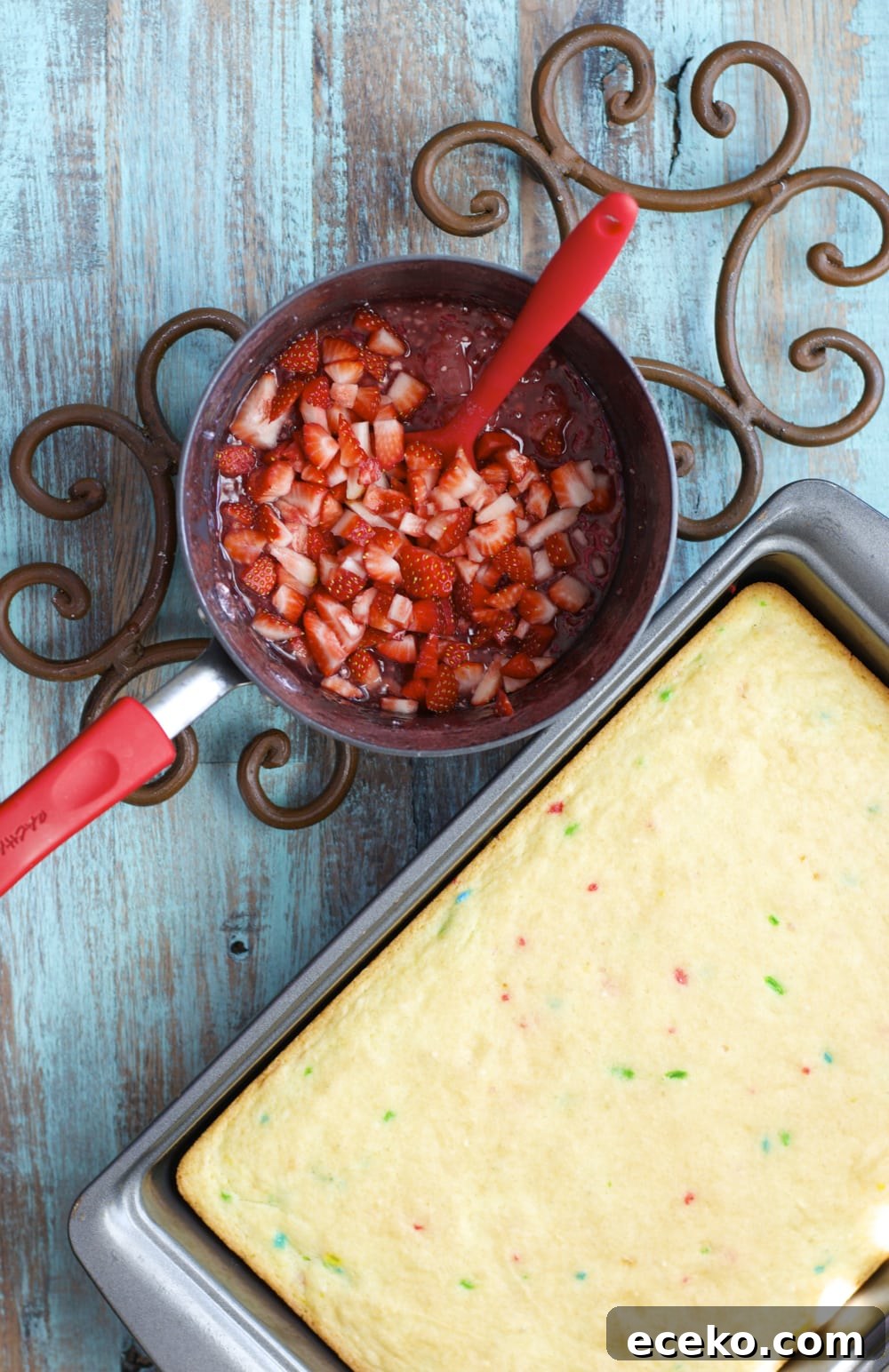 overhead view of gluten free funfetti cake in a baking dish and a saucepan of fresh strawberry sauce