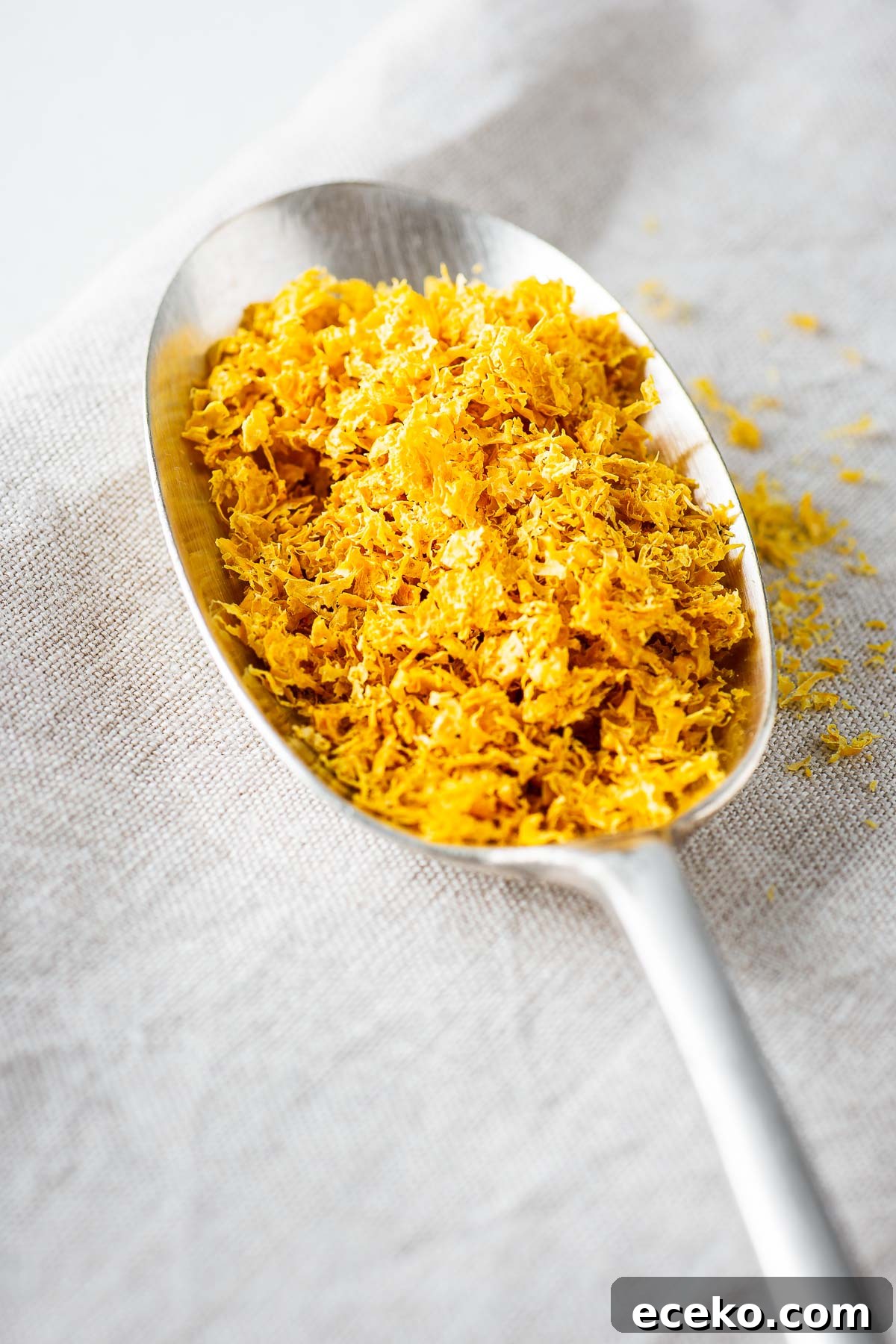 A close-up of a tablespoon of dried lemon zest on a linen background.