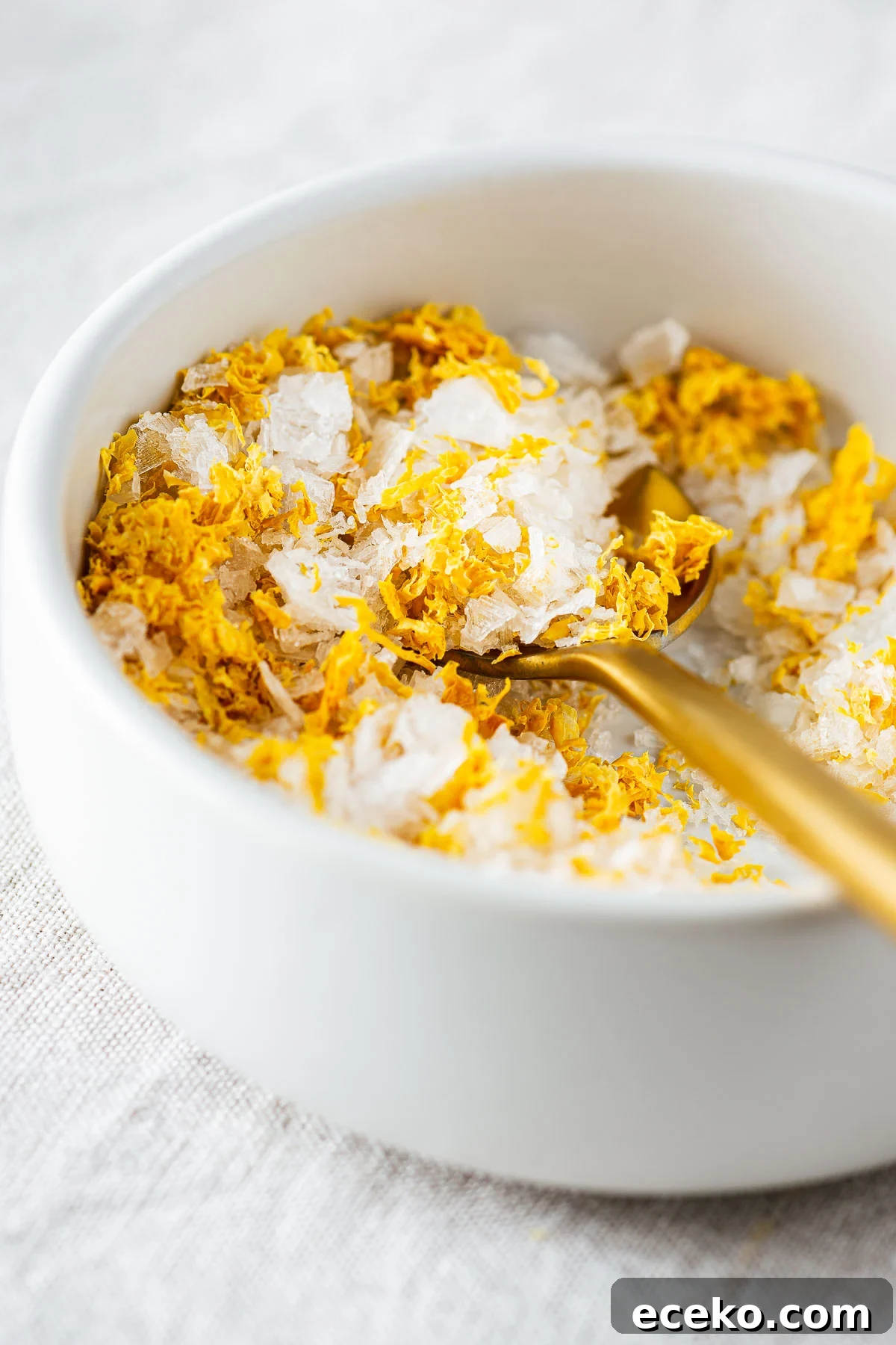 A close-up of a ceramic bowl with of flaked sea salt with dried lemon zest.