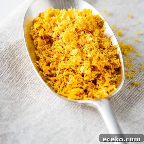 A close-up of a tablespoon of dried lemon zest on a linen background.
