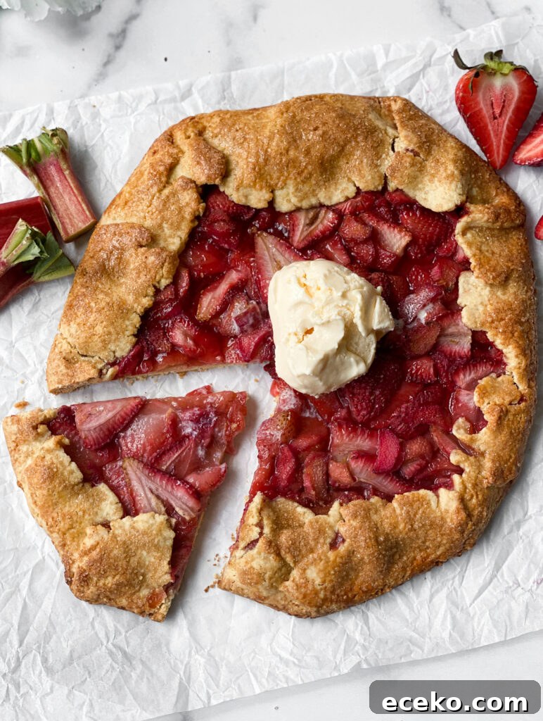 strawberry rhubarb galette with a slice detached and ice cream on top.