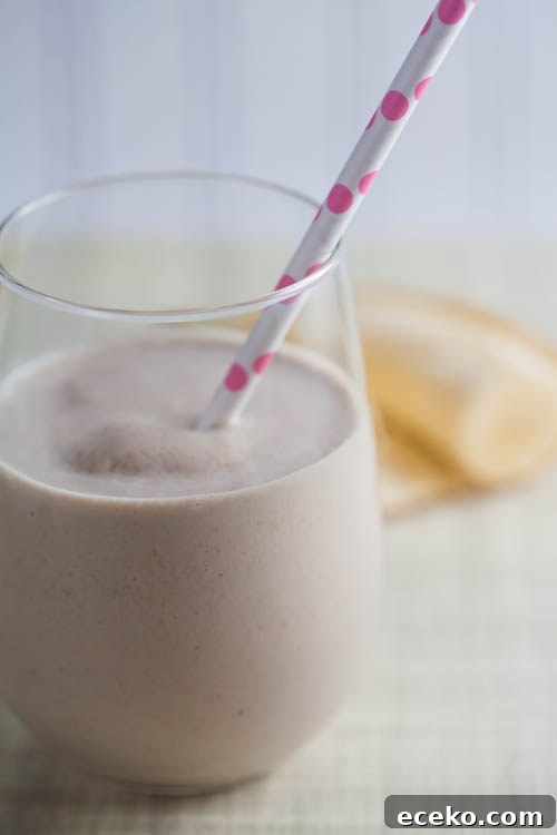 A creamy oatmeal smoothie in a glass, with a pink straw.