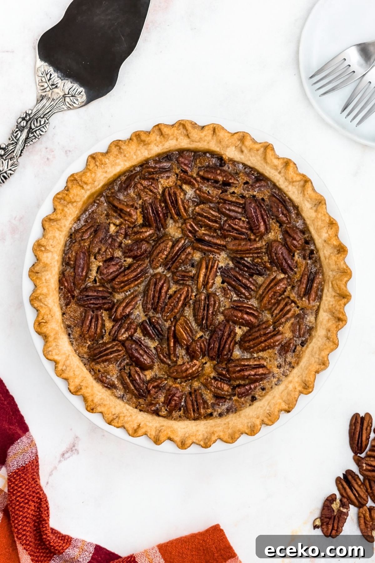 Pecan pie with golden fluted crust on a marble table with spatula and pecans on the table.