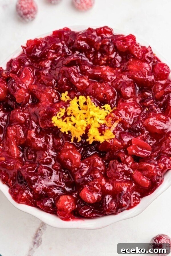 Bright red cranberry sauce in a white bowl, topped with orange zest as a garnish.