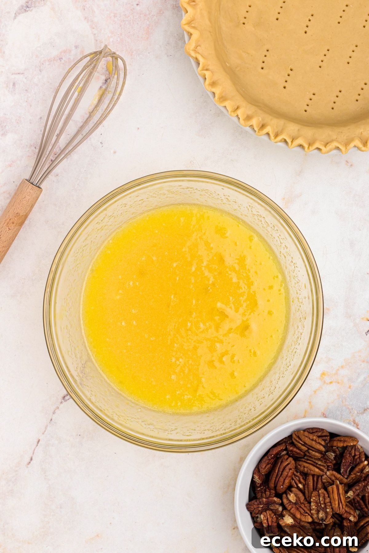 Eggs, sugar, and other pecan pie filling ingredients mixed together in a clear glass bowl.