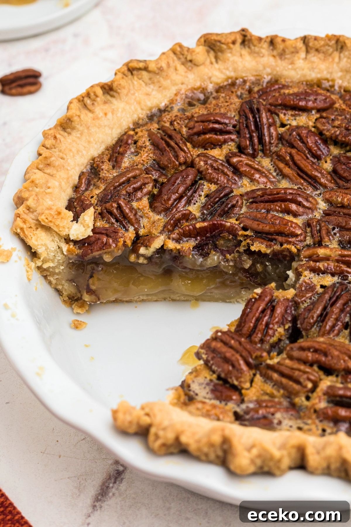 Golden crusted pecan pie with creamy filling and a slice missing, in a white pie plate.