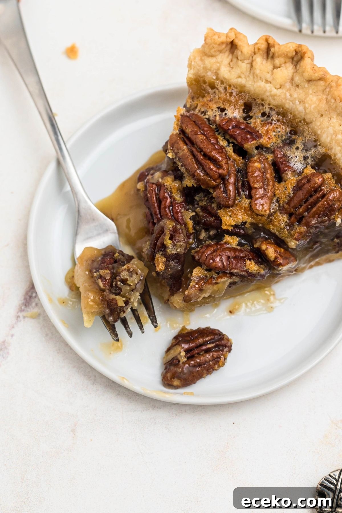 Pecan pie slice on a small white plate with a fork bite shot on the plate.