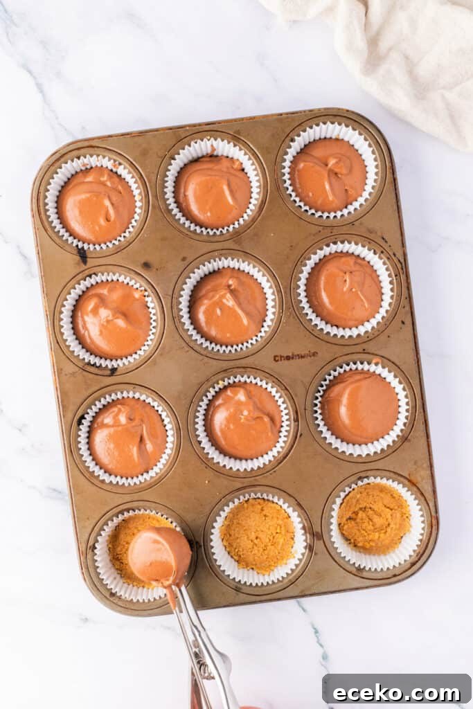 Mini No-Bake Chocolate Peanut Butter Cheesecakes 4 Chocolate cheesecake filling being spooned over graham cracker crust in a lined muffin pan. Some cups are already filled.