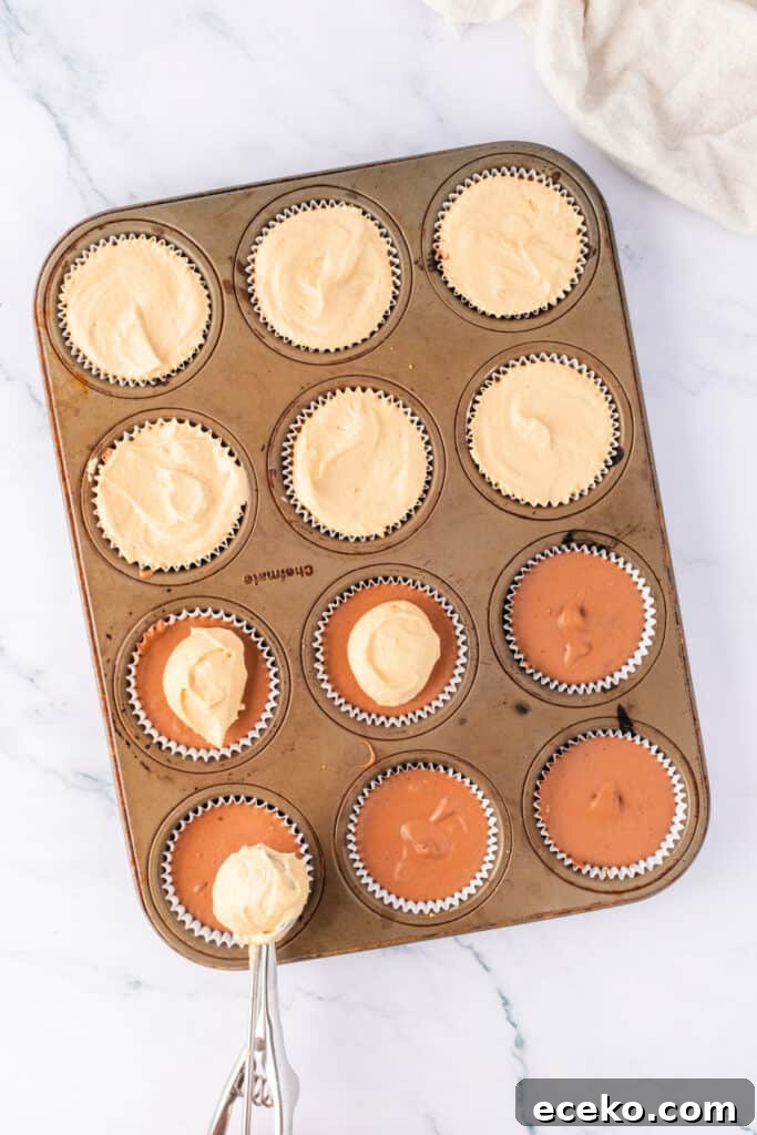 Mini No-Bake Chocolate Peanut Butter Cheesecakes 5 Peanut butter cheesecake layer being added over the chocolate layer in a lined muffin pan using a cookie scoop.