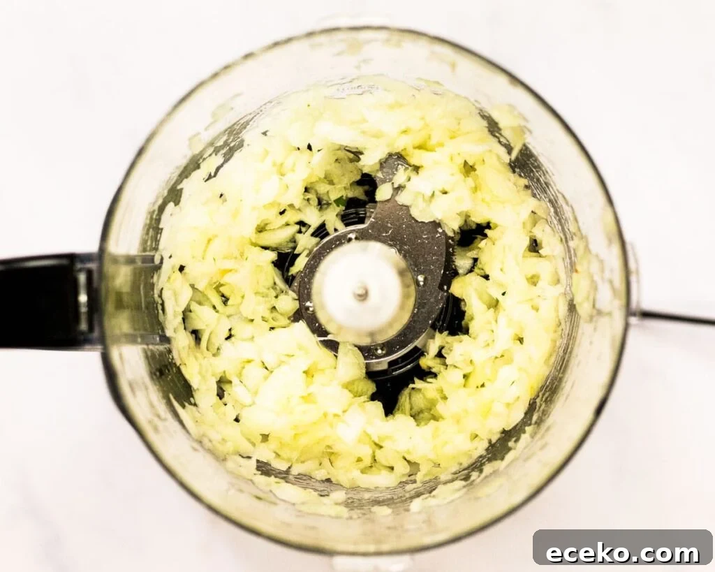 A top down view of chopped onion and garlic in a food processor.