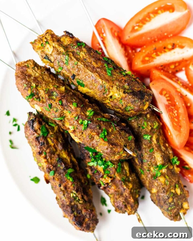 a top down view of a plate of beef kofta kebabs with sliced tomatoes.