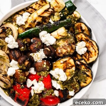 a top down view of a platter of grilled vegetable salad with pesto and goat cheese.