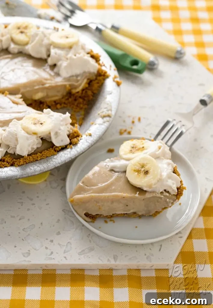 close up of slice of banana cream pie on a white place next to the whole pie