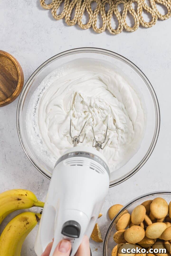 Whipping cream being blended with a hand mixer in a large glass bowl.
