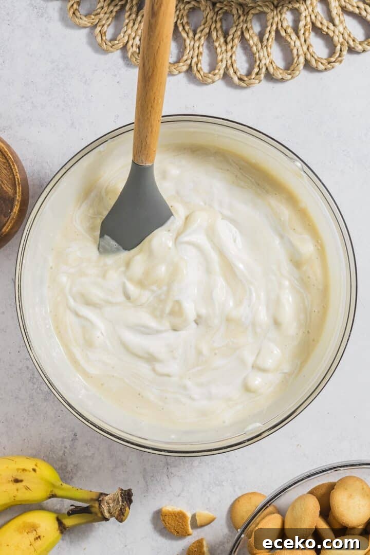 Whipped cream mixed with banana pudding in a large glass mixing bowl.