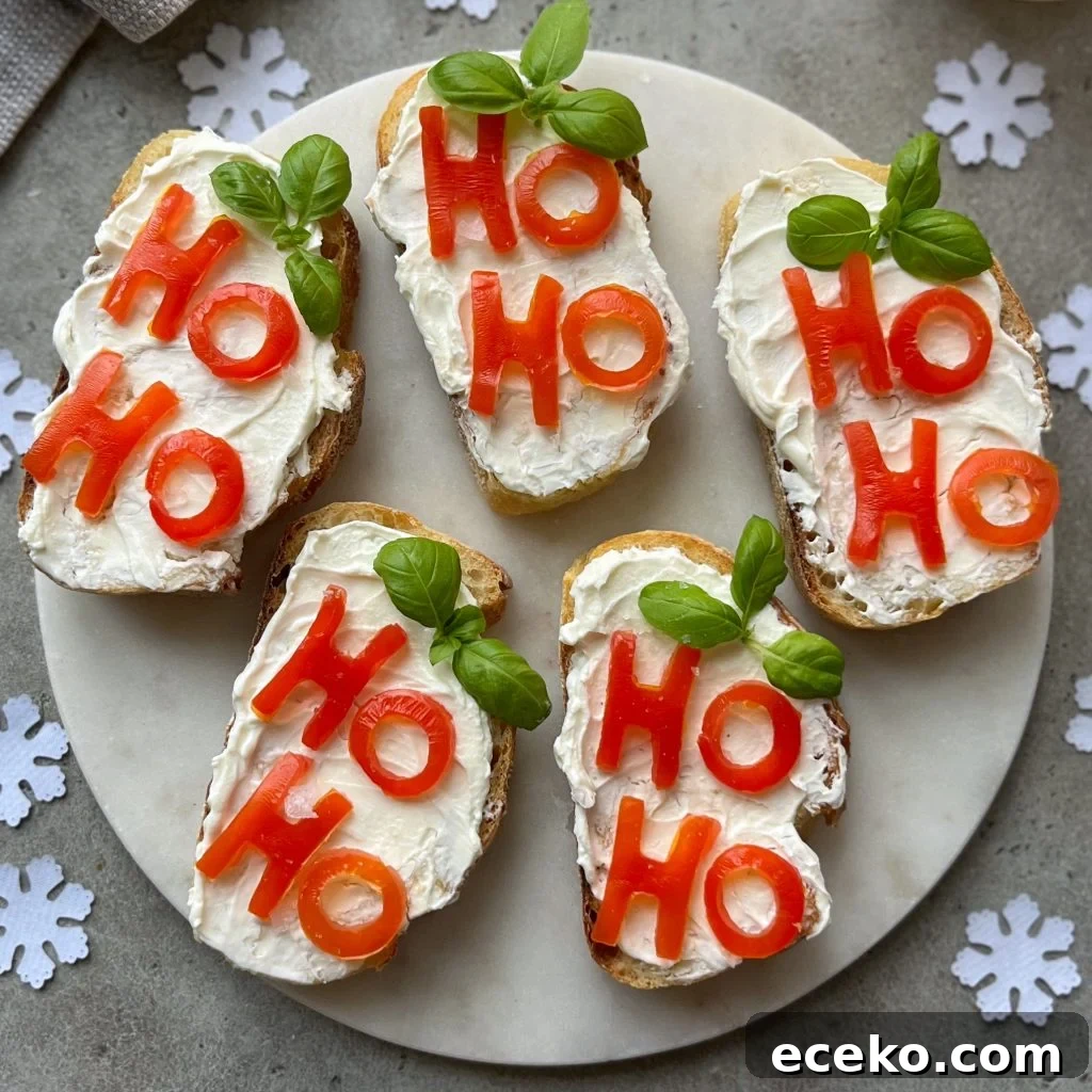 Festive Holiday Appetizers for Entertaining Guests 2 Five slices of Christmas Bruschetta with cream cheese are topped with tomato pieces spelling “HO HO” and garnished with basil leaves, arranged on a white marble plate surrounded by festive paper snowflakes.