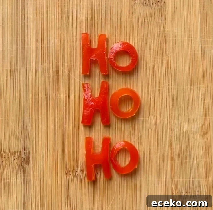 Festive Holiday Appetizers for Entertaining Guests 5 Grape tomato pieces cut into the shape of the letters HO HO HO are arranged vertically on a wooden cutting board.