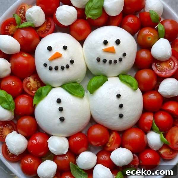 Festive Holiday Appetizers for Entertaining Guests 7 A plate with two snowmen made from burrata balls decorated with peppercorns, carrot slices, basil scarves, and surrounded by cherry tomatoes and more mozzarella balls .