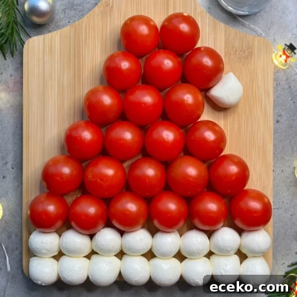 Festive Holiday Appetizers for Entertaining Guests 8 A Santa hat shape made from rows of cherry tomatoes and mozzarella balls on a wooden board.