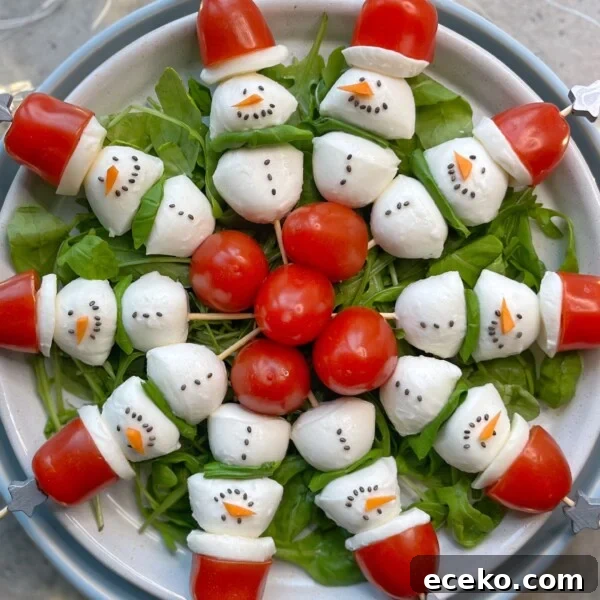 Festive Holiday Appetizers for Entertaining Guests 9 A plate of salad arranged with mozzarella and tomato snowmen, each with black dots for eyes and mouth, and a carrot nose, on a bed of greens—fun bites that make healthy food recipes festive. Cherry tomatoes form Santa hats at the center of the dish.