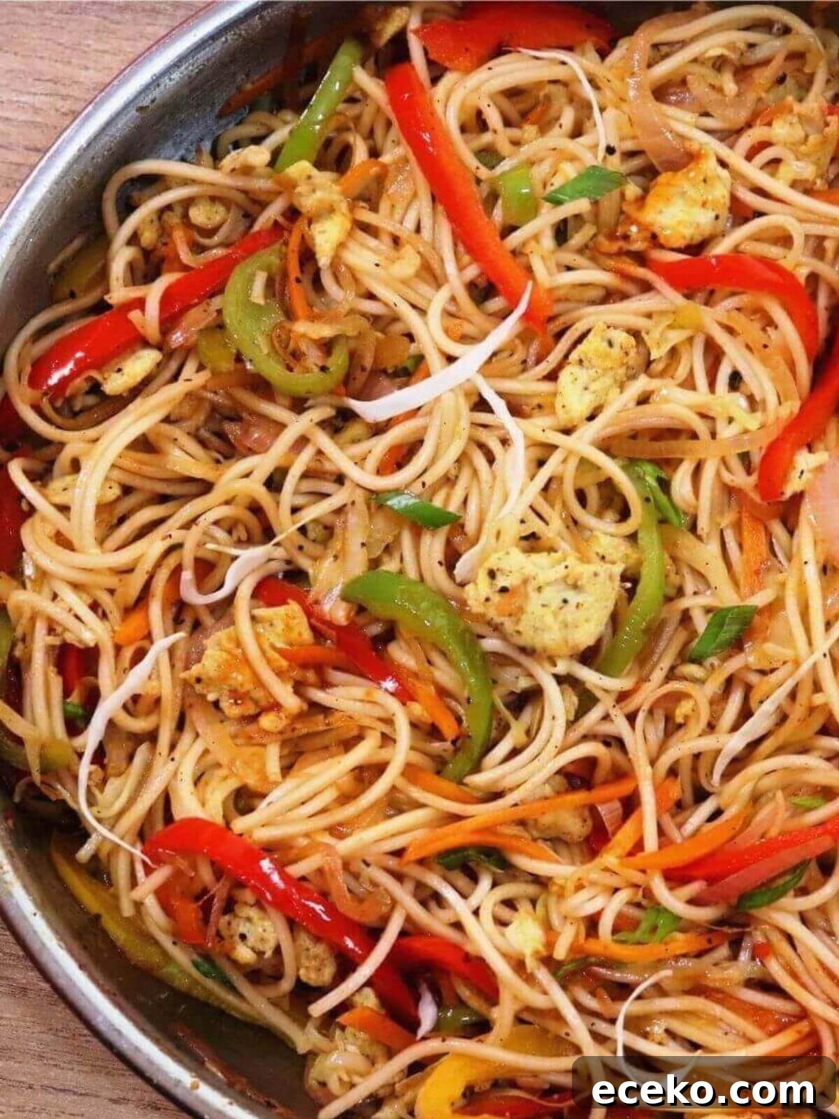 A tight close-up of egg Hakka noodles in a skillet, with only half the skillet visible in the image.