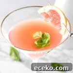 A basil grapefruit martini garnished with a slice of grapefruit, on a white marble table.