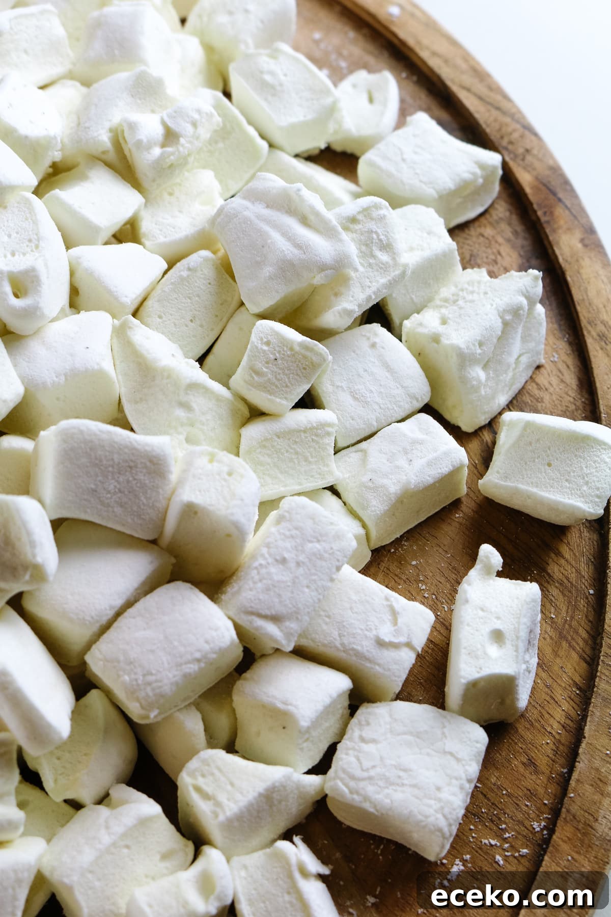 Homemade Marshmallows Without Corn Syrup — Simple Recipe 2 bite sized marshmallows up close on a circular wooden cutting board.