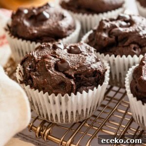 A batch of chocolate avocado muffins on a baking rack with cut up avocado beside them.