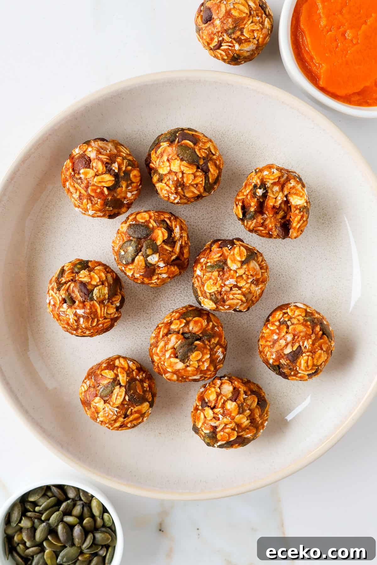 Pumpkin protein balls in a bowl with pumpkin puree and pumpkin seeds on the side. One ball has a bite.