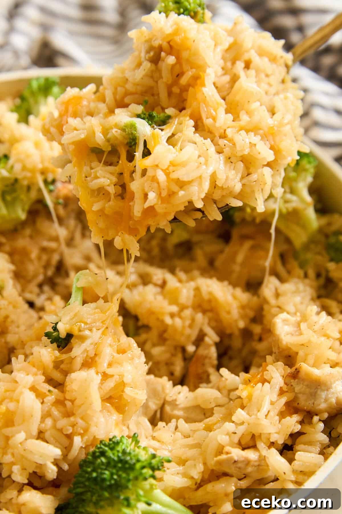 Fixing Gummy Rice: Simple Tips for Fluffy, Separated Grains 2 Close-up of a spoon lifting cheesy rice with broccoli out of a dish, with melted cheese stretching from the spoonful. Rice and broccoli are mixed together, and cheese is visible throughout the dish.