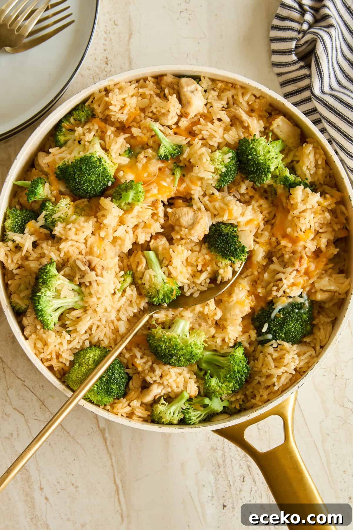 Fixing Gummy Rice: Simple Tips for Fluffy, Separated Grains 4 A skillet filled with rice, broccoli florets, and pieces of chicken, with a gold serving spoon resting inside. A striped cloth and stacked plates with forks are nearby on a light surface.