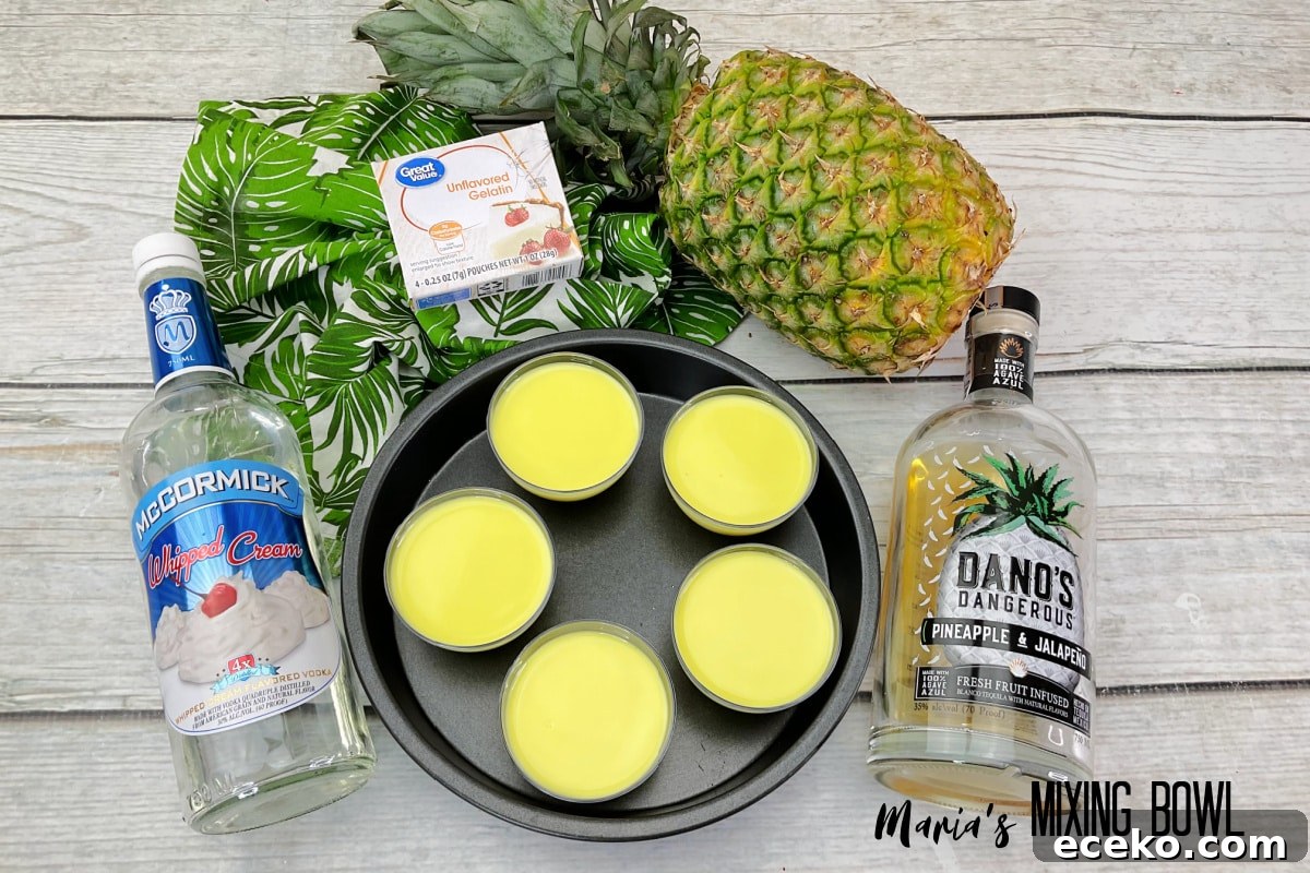 Dole Whip Shot Recipe: How to Make the Creamy Tropical Cocktail 5 five shots of dole whip in a cake pan, surrounded by bottles of alcohol, gelatin, and pineapple