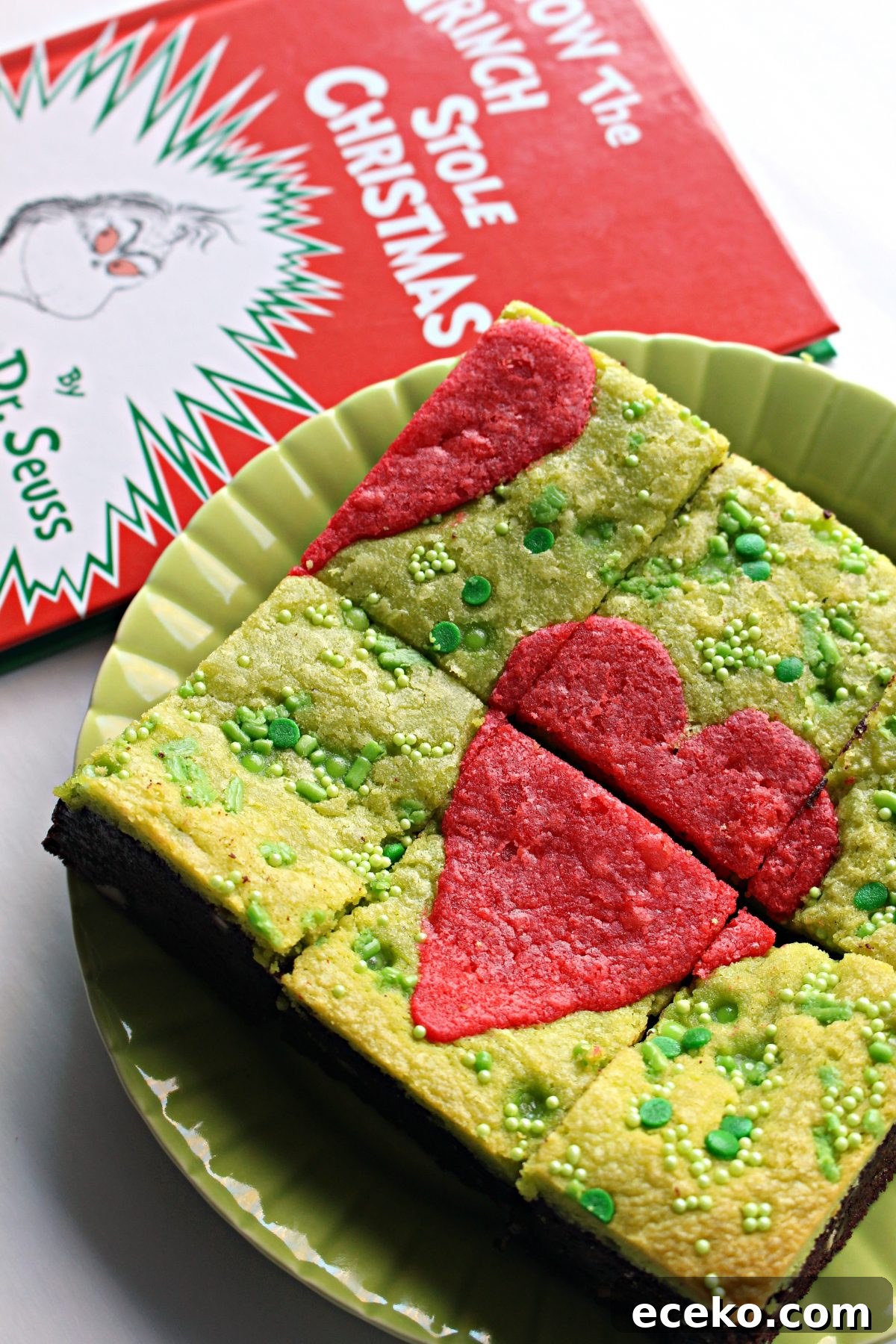 Green Grinch Brownies with a red heart on top on a green plate next to book.