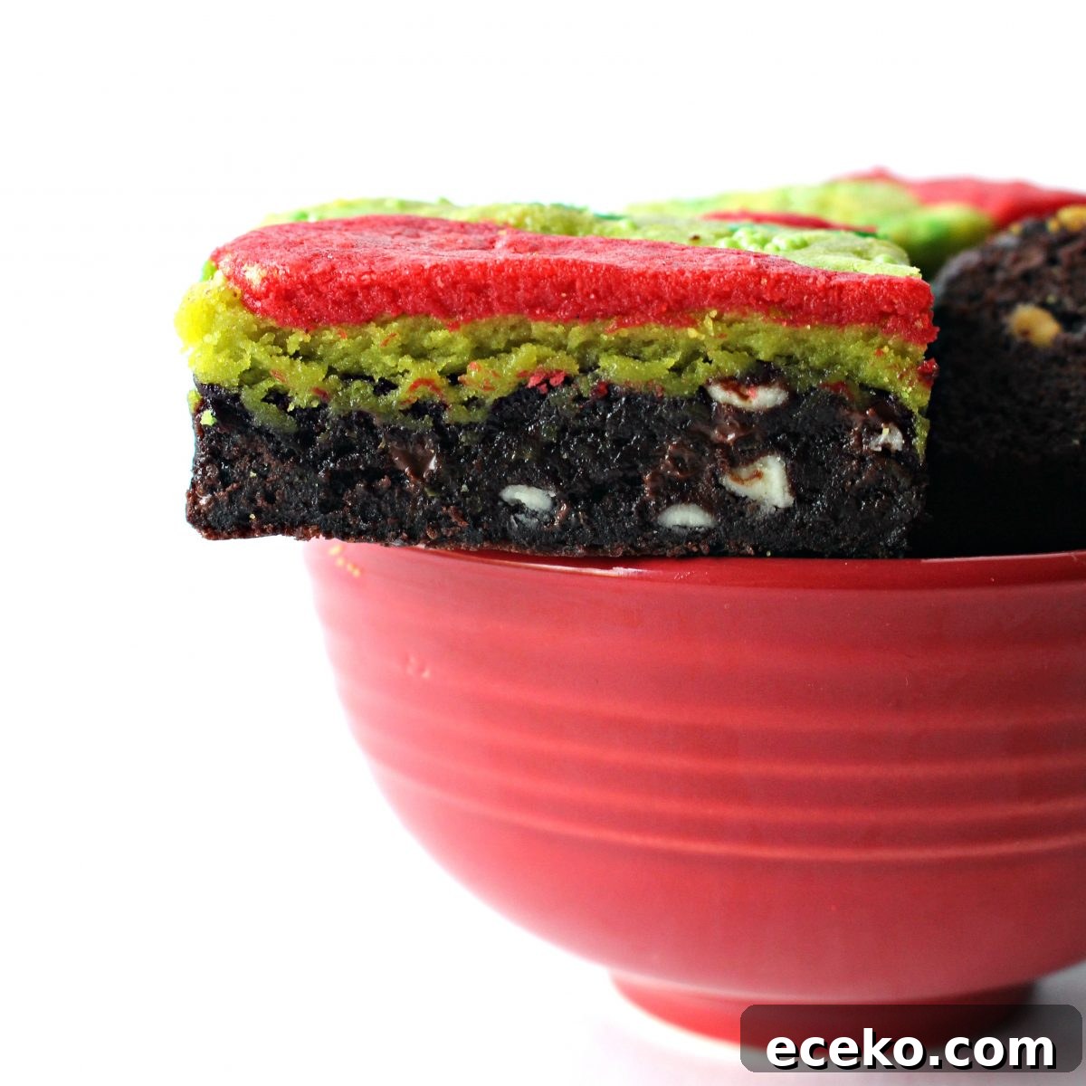 Brownie on top edge of red bowl showing chocolate bottom layer and green and red top.