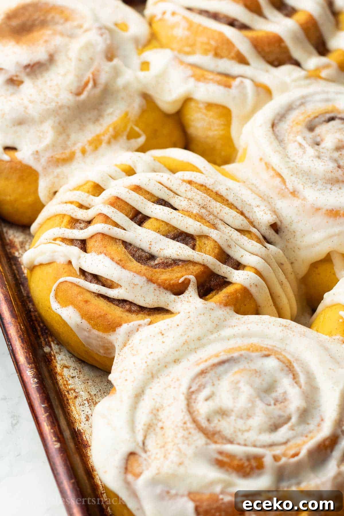 Baked frosted pumpkin cinnamon rolls in metal pan.