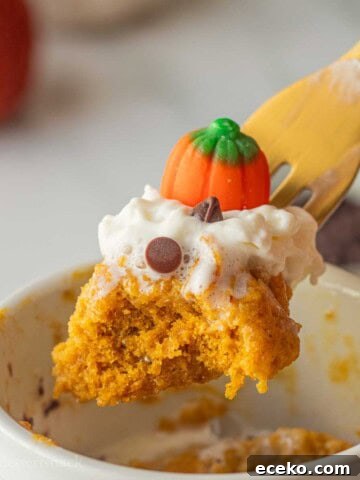 Bite of spiced pumpkin mug cake on gold fork above mug.