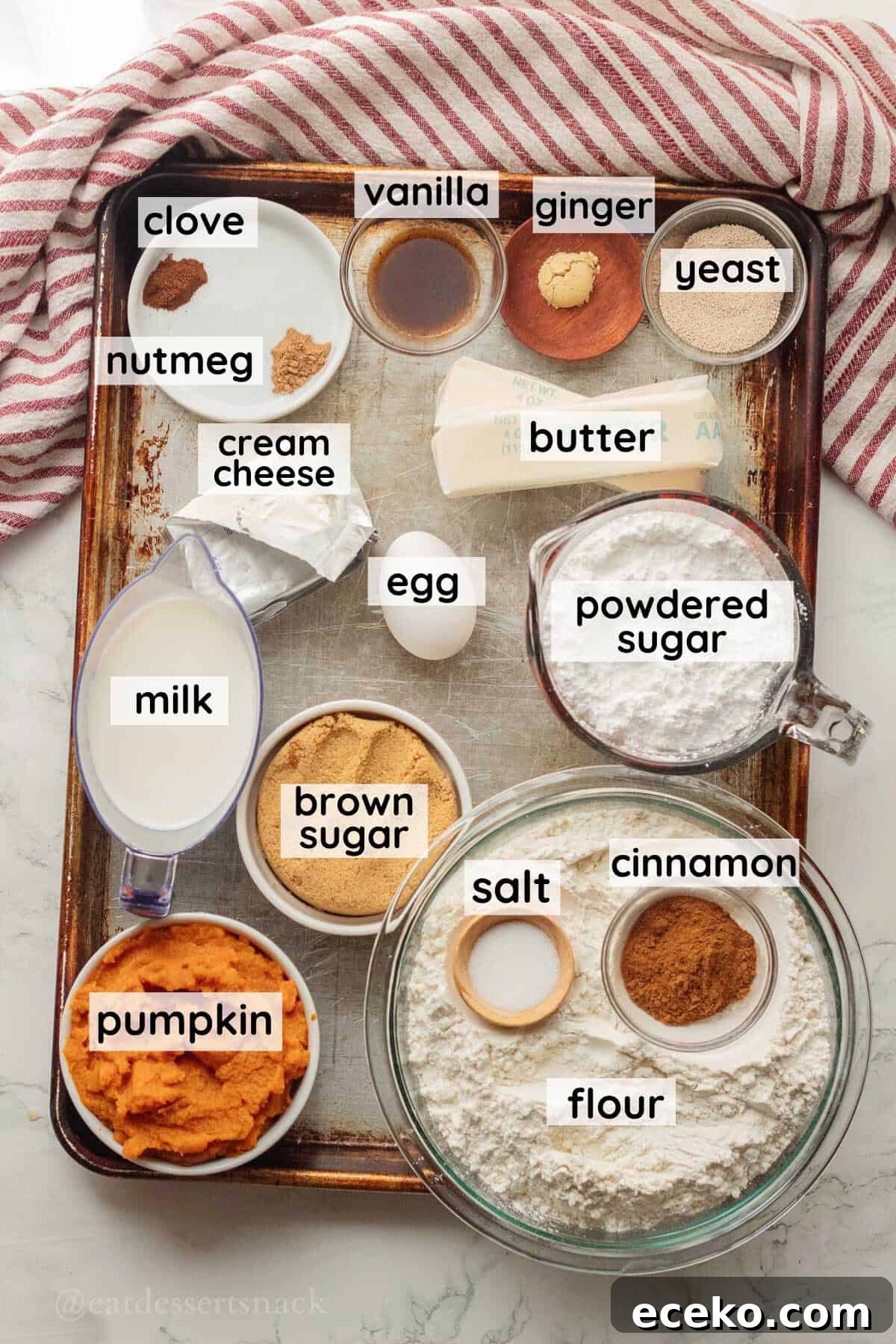 Ingredients for pumpkin cinnamon rolls labeled in glass bowls on metal baking sheet.
