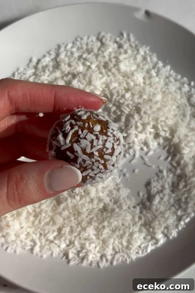 A carrot cake energy ball being rolled into shredded coconut