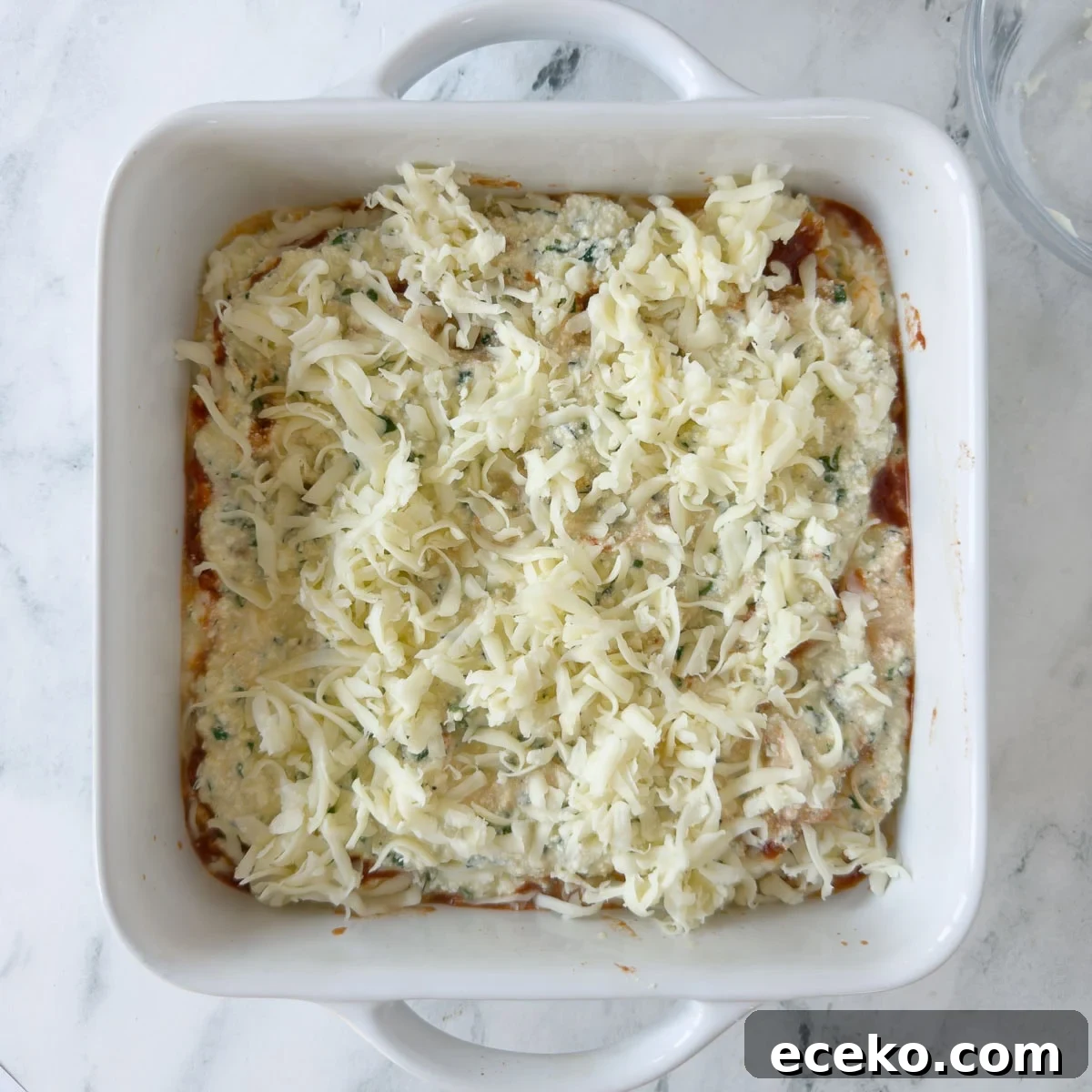 Grate mozzarella cheese on top of noodles and sauce for lasagna.