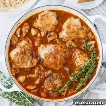 A round pan of golden chicken thighs in red sauce with rosemary on the side.