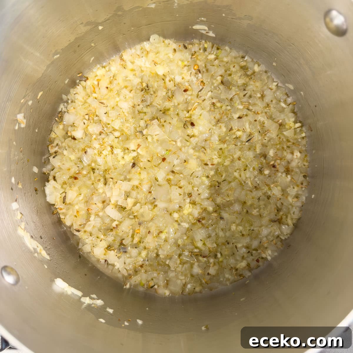 Sautéing onions and herbs in a stainless steel pot.