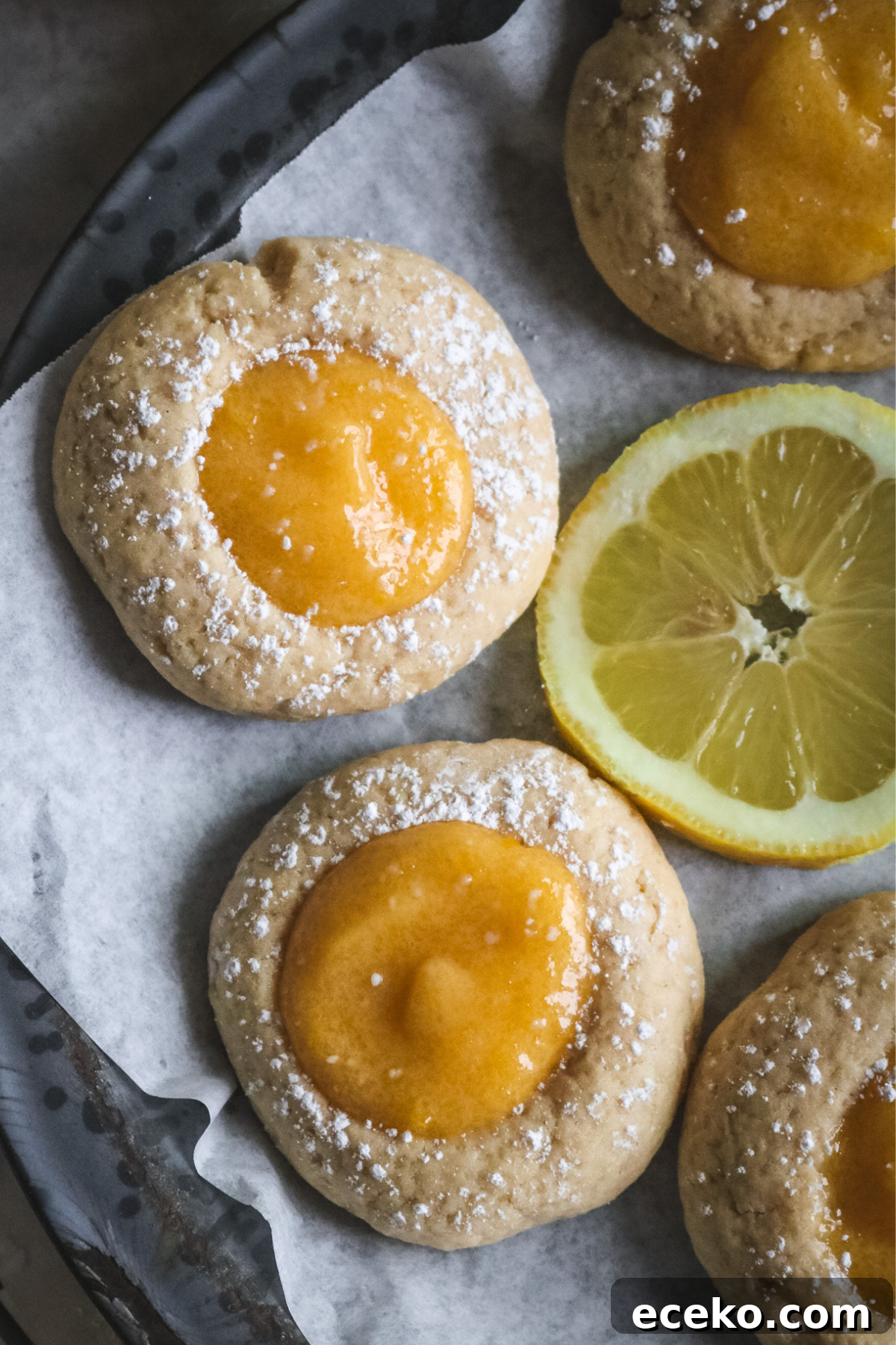 overhead view of chewy lemon curd thumbprint cookies on a gray pie plate lined with parchment paper.