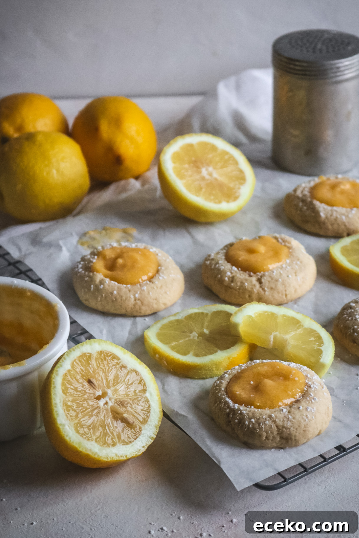 wire rack with parchment paper and fresh lemon curd thumbprint cookies next to sliced lemons.