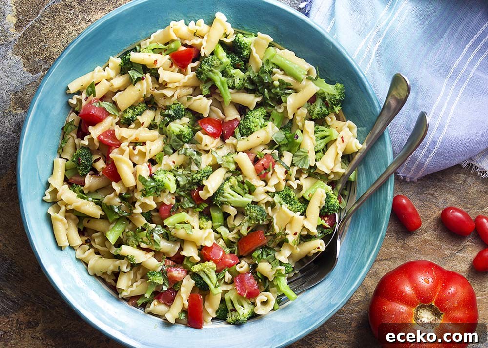 Top view of a large serving bowl of pasta with broccoli and tomatoes.