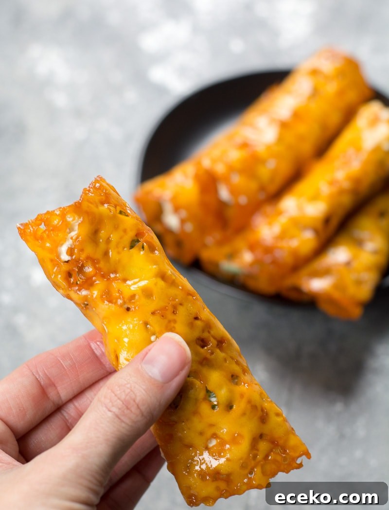 Keto Jalapeño Popper Taquitos with Crispy Bacon 4 a keto jalapeño popper being held aloft over a plate of homemade taquitos