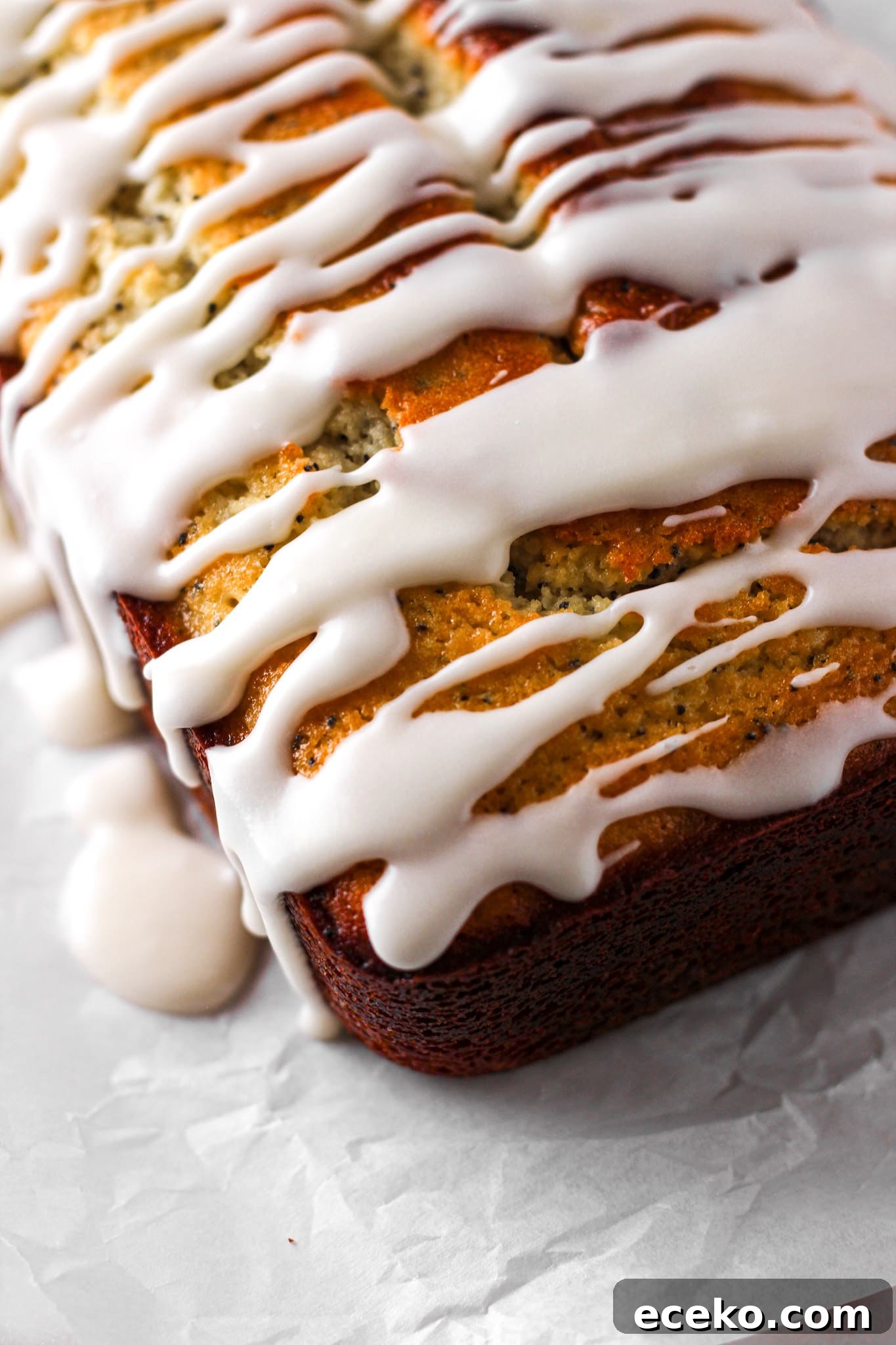 Moist Lemon Pound Cake with Zesty Lemon Glaze 6 close up of a lemon glazed loaf on parchment paper for baked abundance blog