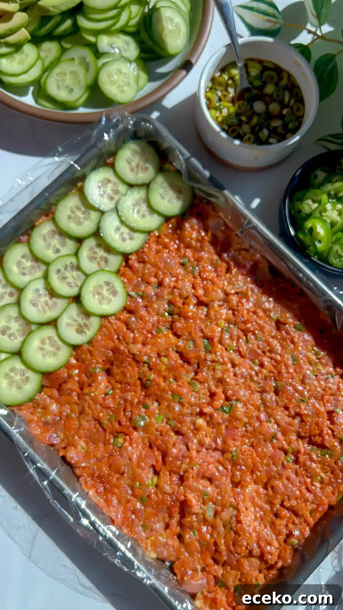 Spicy Tuna Oshizushi: Pressed Sushi Recipe 3 Cucumber rounds layered over gochujang spicy tuna in a plastic wrap lined sheet pan for pressed sushi.