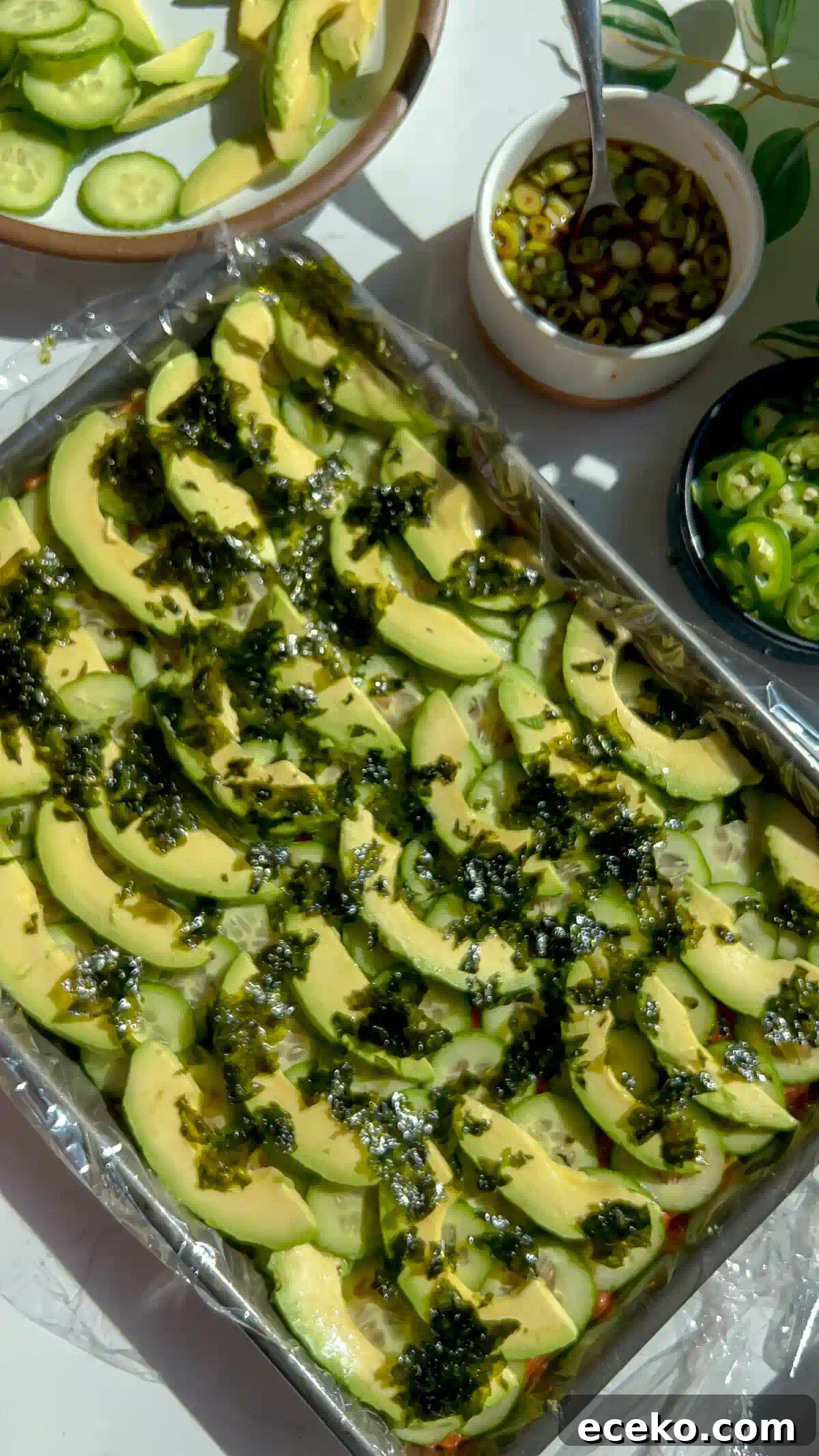 Spicy Tuna Oshizushi: Pressed Sushi Recipe 4 Avocado slices and crumbled nori layered over cucumber in a sheet pan of spicy tuna pressed sushi.
